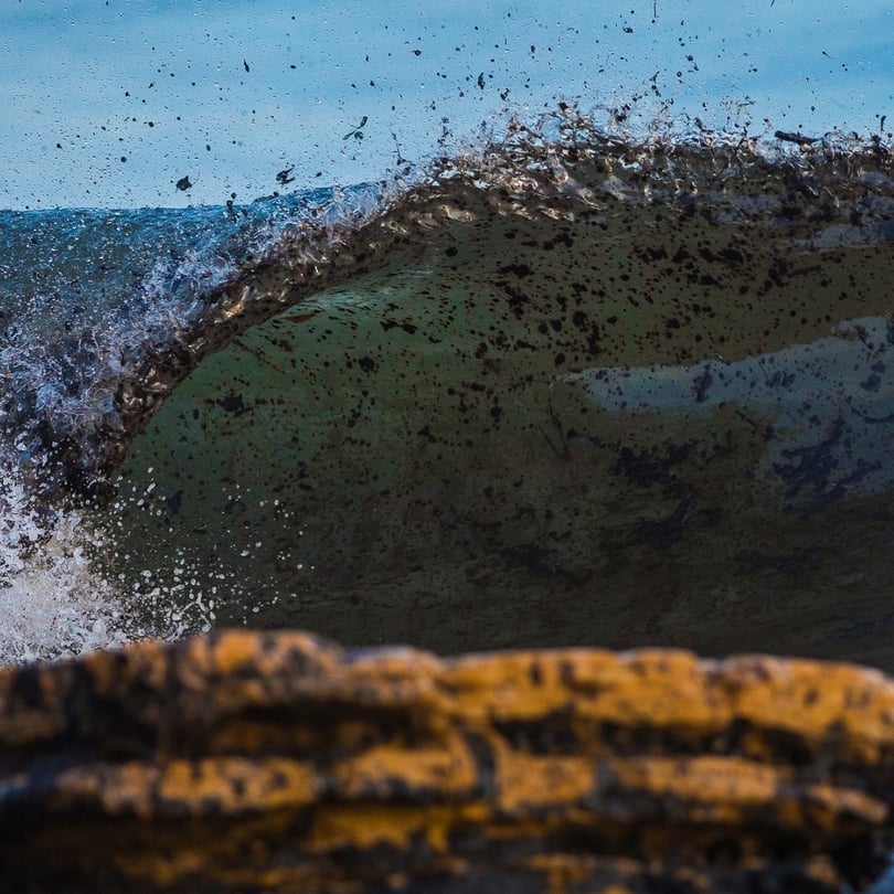 A wave breaks and oil is clearly visible throughout the water.
